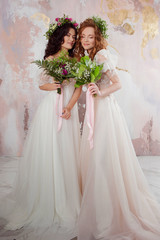 Two charming brides in beautiful spring wreaths on their heads. Beautiful young women in wedding dresses