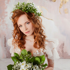 Portrait of a young beautiful woman in wedding dress with wreath and bouquet of fresh flowers.