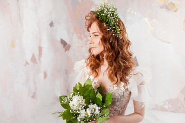 Portrait of a young beautiful woman in wedding dress with wreath and bouquet of fresh flowers.