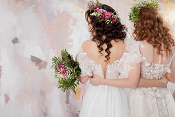 Two charming brides in beautiful spring wreaths on their heads. Beautiful young women in wedding dresses