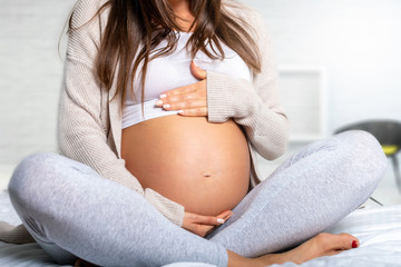 Schwangere Frau hält ihren nackten Bauch und sitzt zu Hause auf dem Bett