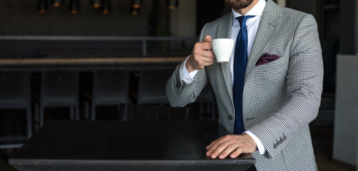 Man in expensive custom tailored suit standing and drinking coffee and posing indoors