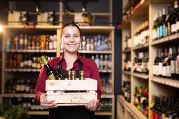 Photo of young brunette seller with wooden box with wine in store
