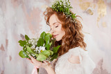Portrait of a young beautiful woman in wedding dress with wreath and bouquet of fresh flowers.
