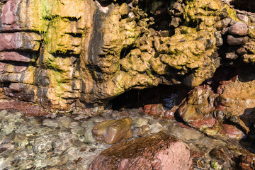 on the shore of the sea is a rock over which the running water has been colored in yellow; next to the red rocks
