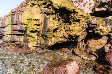 on the shore of the sea is a rock over which the running water has been colored in yellow; next to the red rocks