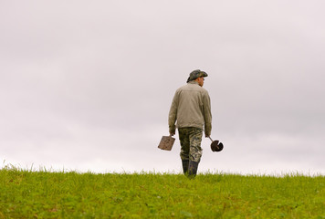 The caucasian geologist is going against the background of the cloudy sky across a field and...