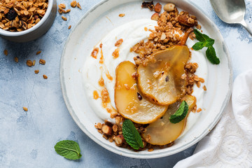 Greek yogurt with caramelized pear, granola, nuts and melted sugar for a wholesome breakfast on a gray ceramic plate. Rustic style. Top view.