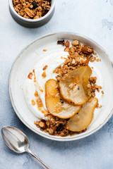 Greek yogurt with caramelized pear, granola, nuts and melted sugar for a wholesome breakfast on a gray ceramic plate. Rustic style. Top view.