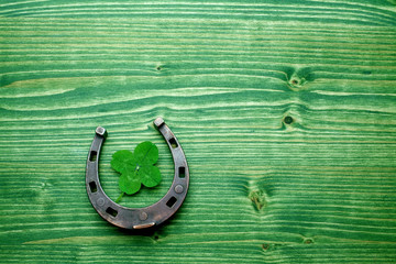 four-leaved clover and a horse shoe on green wooden background. St. Patrick's day