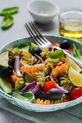 Pasta salad with colorful fusilli and vegetables in a ceramic plate. Top view.