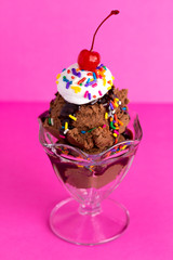 A Chocolate Sundae with Sprinkles and a Cherry on a Pink Background