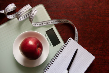 The concept of healthy nutrition, fitness and weight loss. Weights, measuring tape, apple, open notebook and pencil on the table.