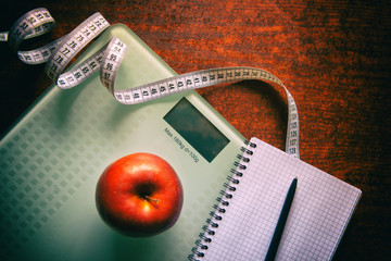 The concept of healthy nutrition, fitness and weight loss. Weights, measuring tape, apple, open notebook and pencil on the table.