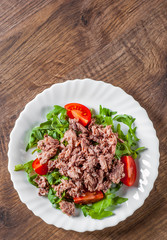 Tuna salad with arugula and tomatoes in white plate on wooden table background