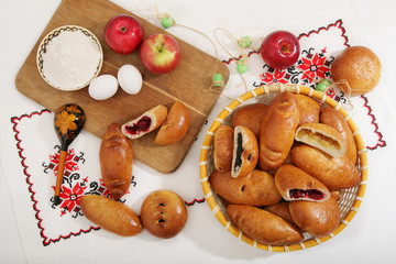 Still-life with traditional Russian pies, ingredients - flour, eggs, apples. On authentic tablecloth with a wooden spoon with a pattern