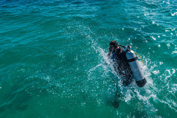 Male scuba diver with equipment jumps in water