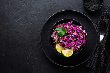 Salad of purple Peking cabbage with olive oil, lime and black sesame seeds in ceramic plate on dark concrete background.