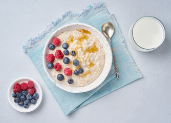 Oatmeal with berries, chia, maple syrup and glass of milk on blue light background. Top view. Healthy diet breakfast