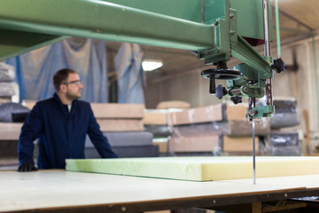 Young man in a furniture factory is cutting the foam for the sofa