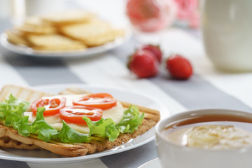 Fresh, tasty breakfast with a sandwich and tea on a light background.