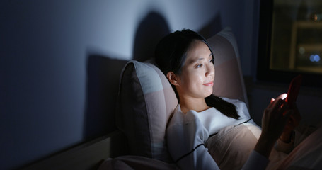 Obraz premium Woman use of mobile phone on bed at night