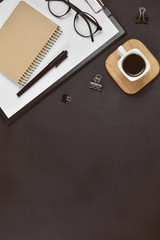 Mock up workspace with blank clip board, office supplies, pen, coffee cup, notepad and eyeglasses on dark background. Flat lay, top view, copy space