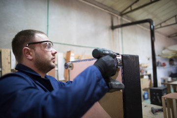 Young man in a furniture factory attaches the sofa leg