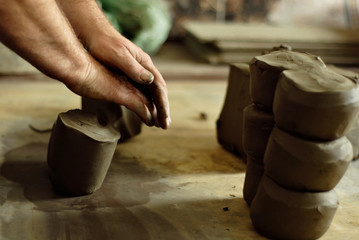The man carves an ornament on an earthenware bowl. Handmade products on the table at home workshop.