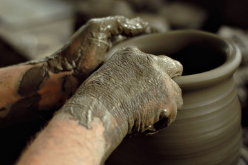 The man carves an ornament on an earthenware bowl. Handmade products on the table at home workshop.
