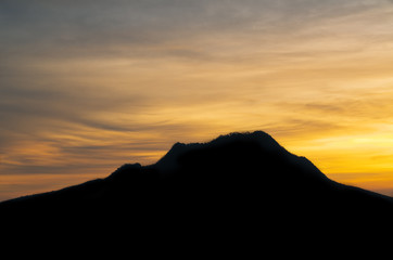 Scenic sunset landscape with golden sunlight above silhouette of mountains and clouds at the sky.
