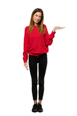 A full-length shot of a Young woman with red sweater holding copyspace imaginary on the palm to insert an ad over isolated white background