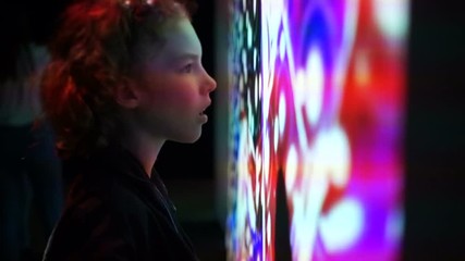 Curly schoolboy looks at the interactive wall with abstract patterns. The boy is surprised and fascinated. Children and technology of the future
