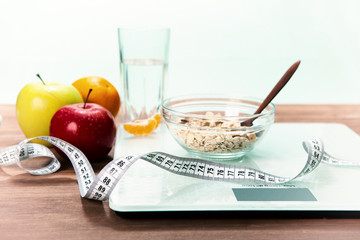 Healthy diet, fitness and weight loss concept. Scales, measuring tape, oatmeal, apple, a glass of water, an open notebook and a pencil on the table.
