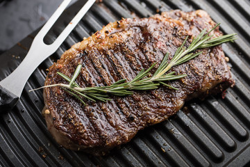 Roasted steak meat with rosemary leaves on grill grid