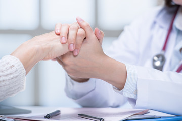 Medical doctor reassuring patient by holding patient’s hands in hospital setting