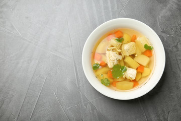 Homemade chicken soup in dish on grey background, top view with space for text