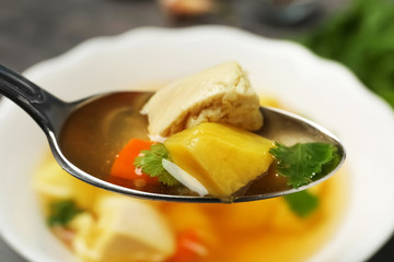 Spoon with fresh homemade chicken soup on blurred background, closeup