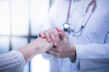 Medical doctor reassuring patient by holding patient’s hands in hospital setting