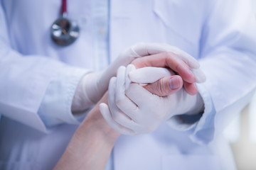 Medical doctor wearing latex gloves holding patient’s hand to give support in hospital setting