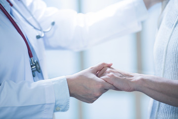 Medical doctor reassuring patient by holding patient’s hands in hospital setting