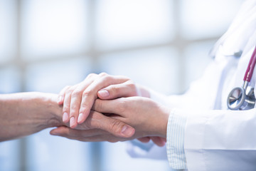 Medical doctor reassuring patient by holding patient’s hands in hospital setting
