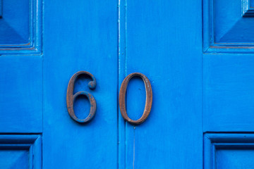 House number sixty in faded bronze numerals on a blue painted wooden house door