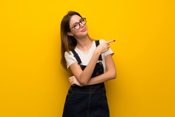 Woman over yellow wall pointing finger to the side