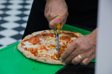 Finished Italian pizza on a thin dough, the chef cut the pizza into pieces for tasting. Selective...