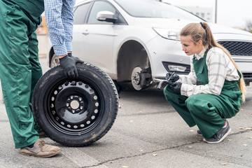 Woman mechanic checking spare wheel near car