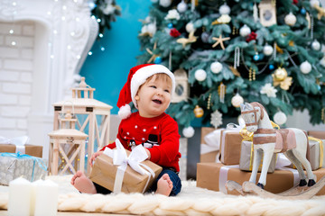 Fototapeta na wymiar little baby santa claus in christmas hat. Happy new year and merry christmas. Holidays and gifts for children
