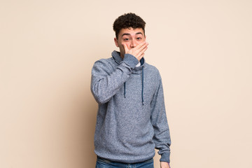 Young man over isolated wall covering mouth with hands