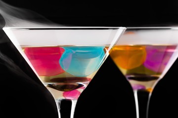 wine glasses with colored ice cubes and floated ice vapor on black background. Selective focus