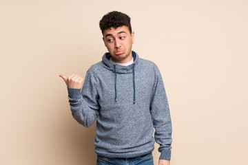 Young man over isolated wall unhappy and pointing to the side